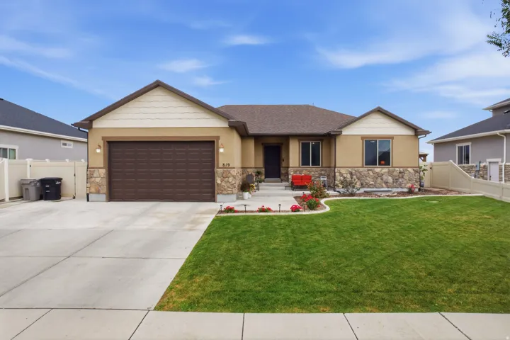 Stucco exterior with stone accents, attached two-car garage, mature landscaping, concrete driveway, and a well-maintained lawn