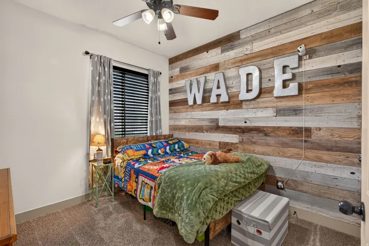 Reclaimed wood accent wall, ceiling fan with integrated lighting, window with blinds, and neutral carpet