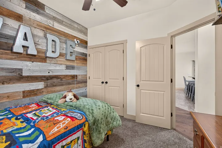 Accent wall with horizontal wood planks, ceiling fan with light fixture, carpeted flooring, arched paneled door, and bi-fold closet doors