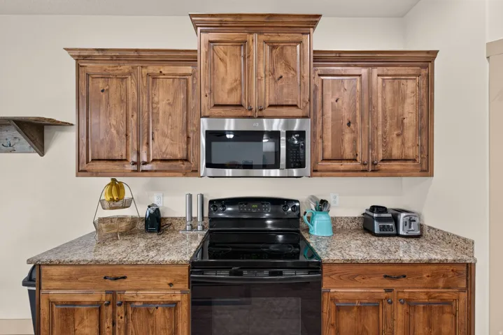 Wood-finish cabinetry with crown molding, stainless steel microwave, black electric range, and speckled countertops