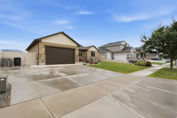 Stucco exterior with stone veneer accents, an attached garage, a paved driveway, and a manicured front lawn