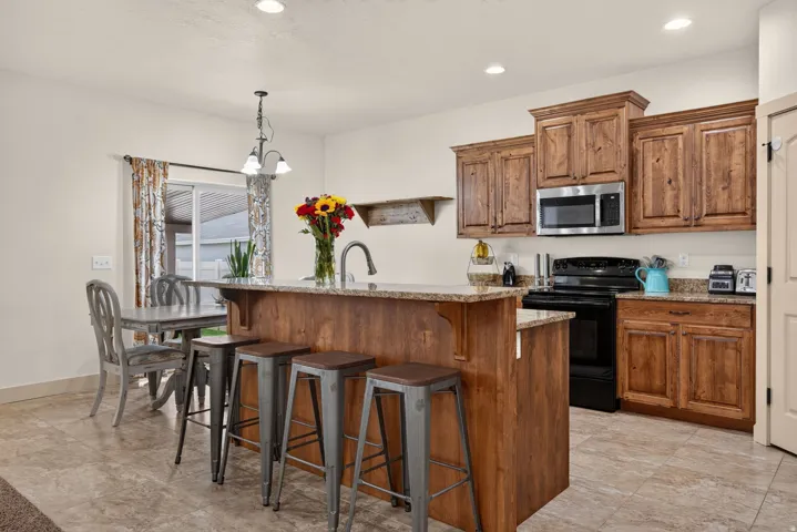 Kitchen featuring wood-finish cabinetry, stainless steel microwave, black range, granite-style countertops, and a kitchen island with seating