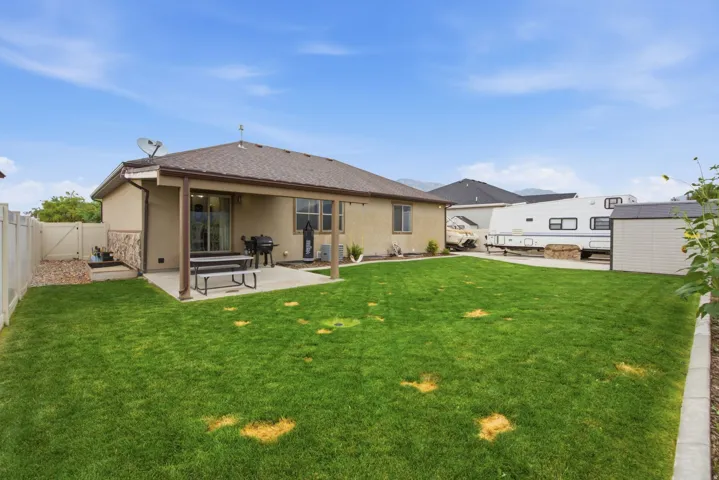 Expansive rear yard featuring a covered patio with concrete flooring, a sliding glass door, a storage shed, and a privacy fence