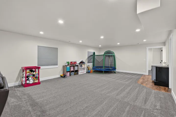 Recessed lighting, light gray wall paint, window with blinds, gray patterned carpeting, and a built-in cabinet with a light-colored countertop