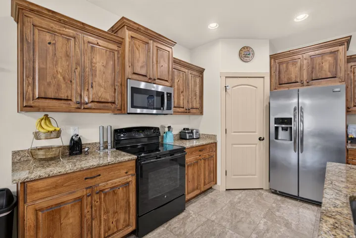 Kitchen featuring wood-finish cabinetry, speckled countertops, stainless steel refrigerator, stainless steel microwave, and a dark-finish electric range