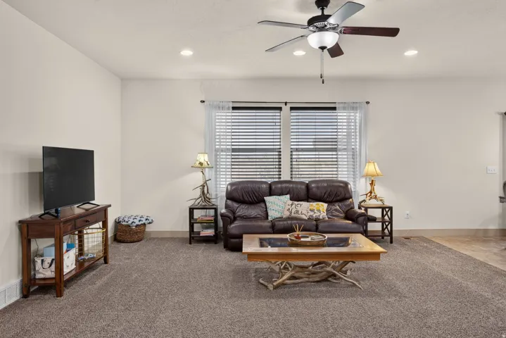 Spacious living area featuring neutral carpeting, a ceiling fan with integrated lighting, and recessed lighting