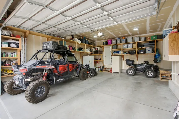 Concrete flooring, overhead garage door, built-in shelving, overhead lighting, and built-in cabinetry