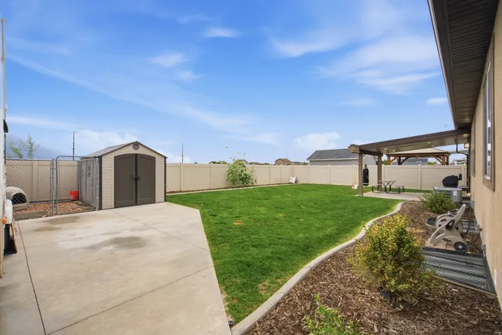Expansive backyard featuring a concrete patio, a storage shed, a manicured lawn, and a covered pergola