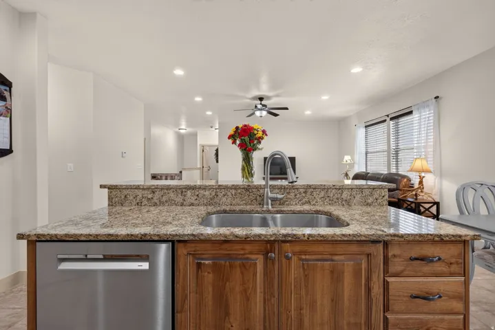 Kitchen island with stone-finish countertops, stainless steel undermount sink, built-in dishwasher, and wood-finish cabinetry