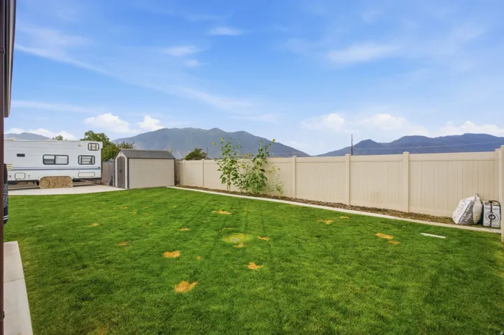 Expansive grassy backyard featuring a storage shed, concrete patio area, and perimeter fencing