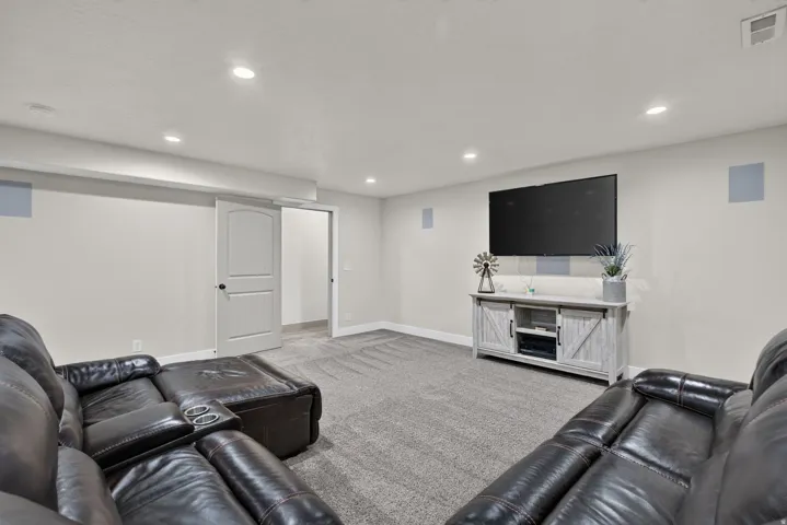 Recessed lighting, light gray wall paint, gray carpeting, white trim, and a white interior door with black hardware
