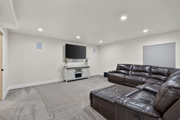 Recessed lighting, wall-mounted speakers, window with cellular shade, light-colored walls, and gray carpeting