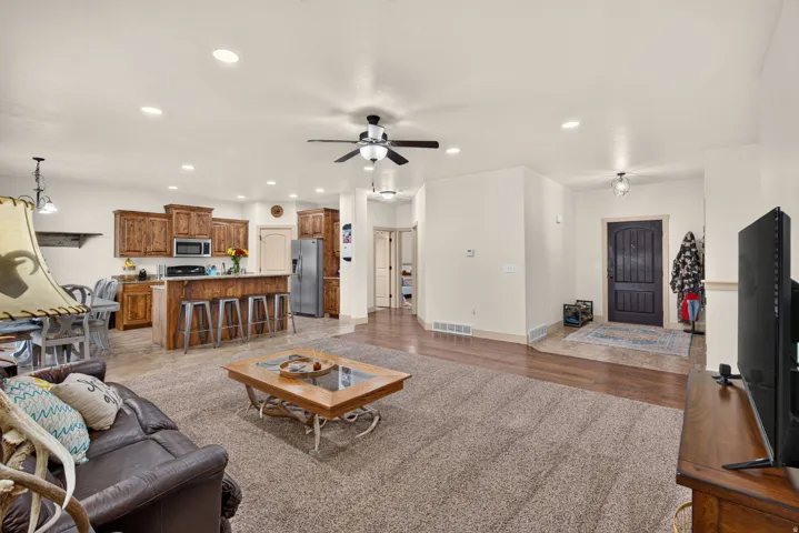 Open-concept living space featuring wood-finish flooring, a kitchen island with seating, recessed lighting, and a ceiling fan