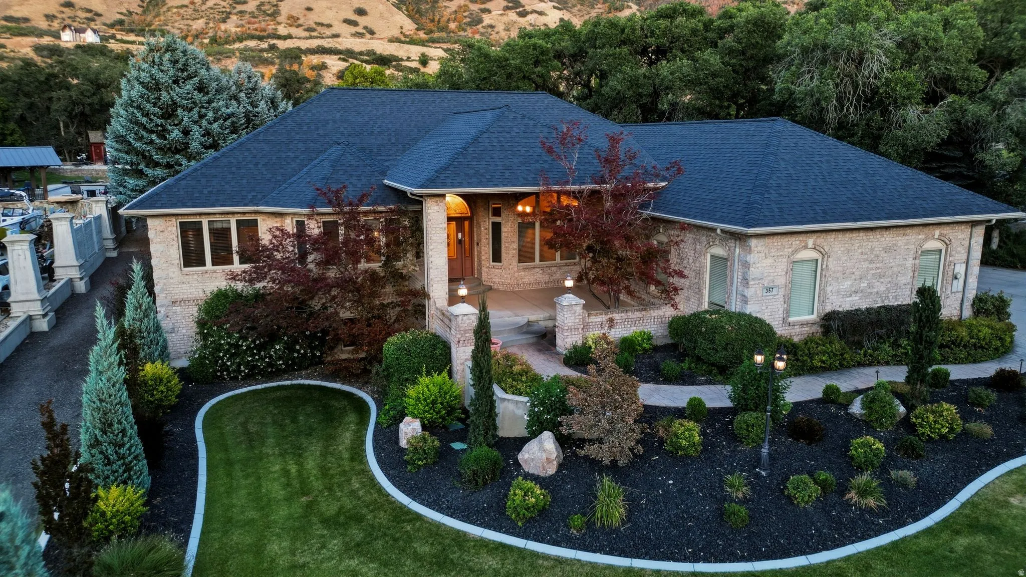 Stone facade residence with a dark shingle roof, extensive landscaping, and a curvilinear lawn