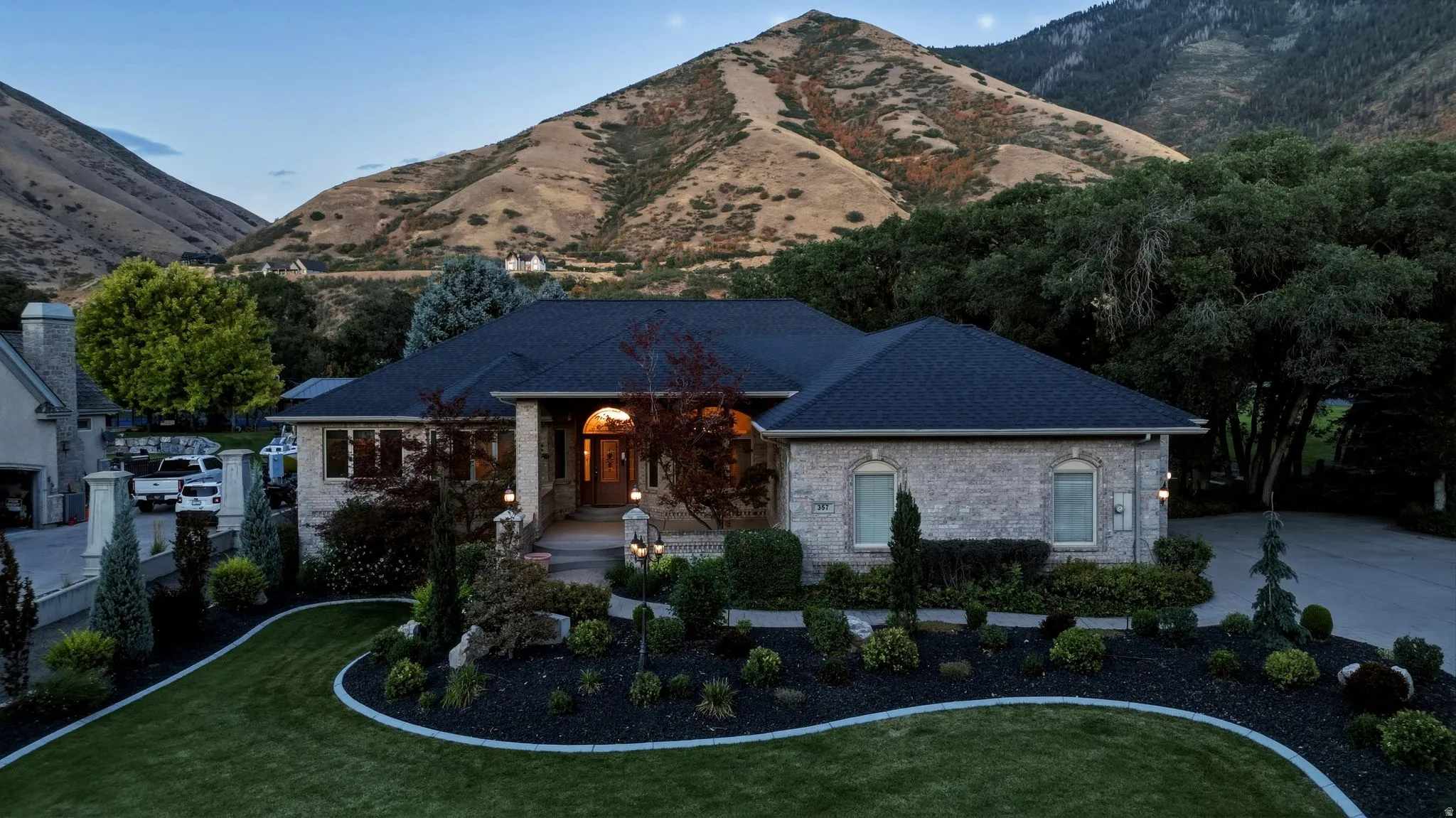 Stone exterior with a dark shingle roof, arched entry, formal landscaping, and a manicured lawn