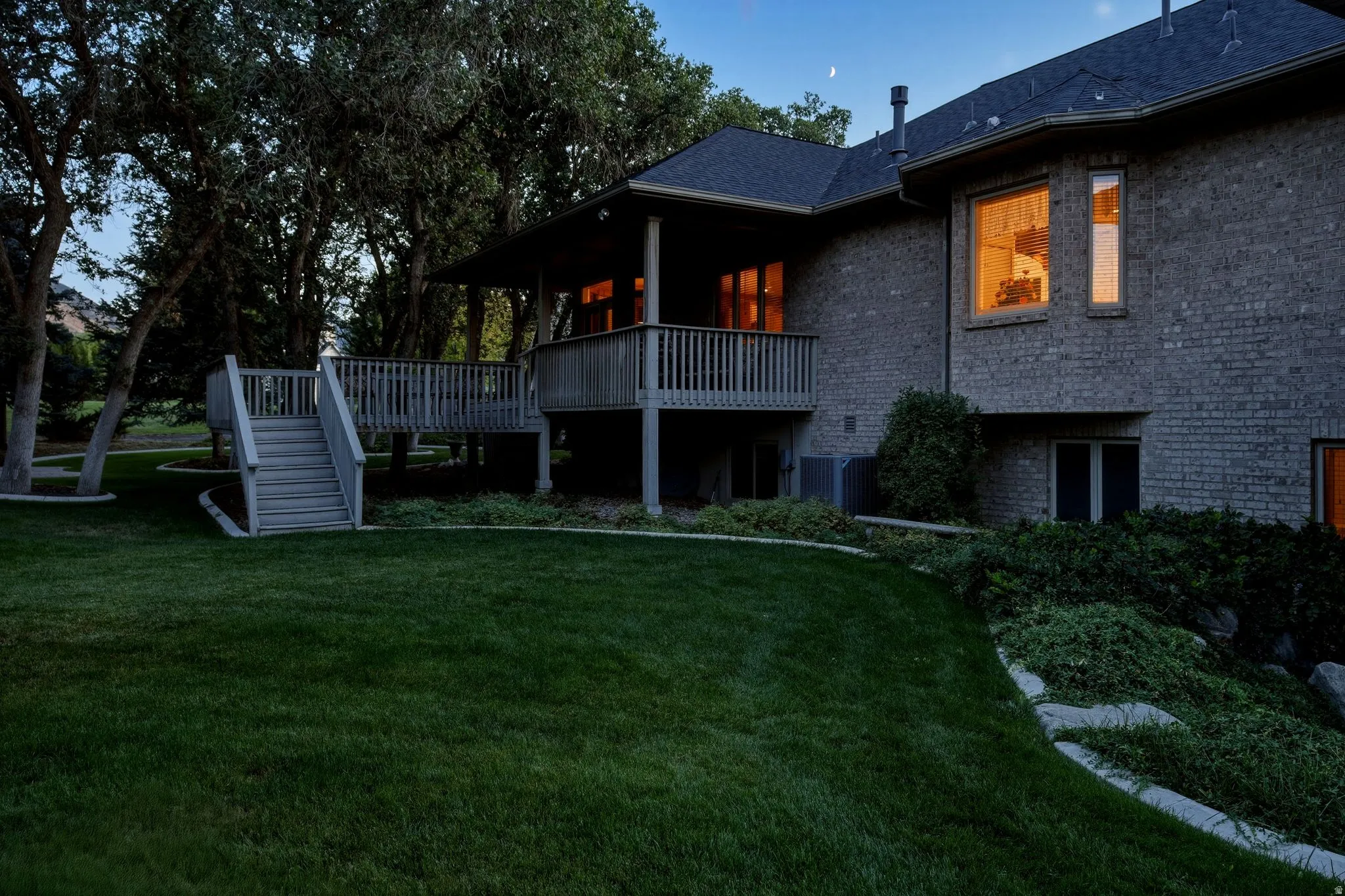 Brick exterior featuring multiple window styles, a raised wood deck with staircase, and sloped, manicured landscaping