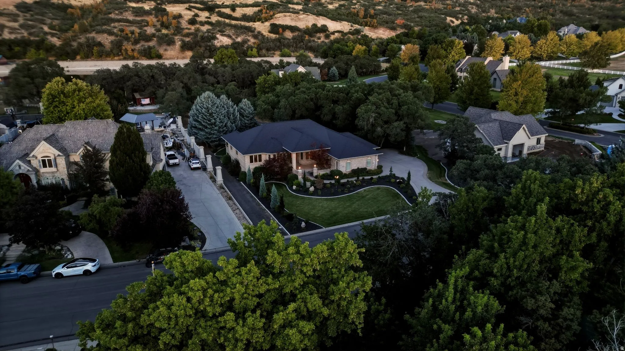 Expansive property featuring a circular driveway, mature trees, manicured landscaping, and a dark shingle roof