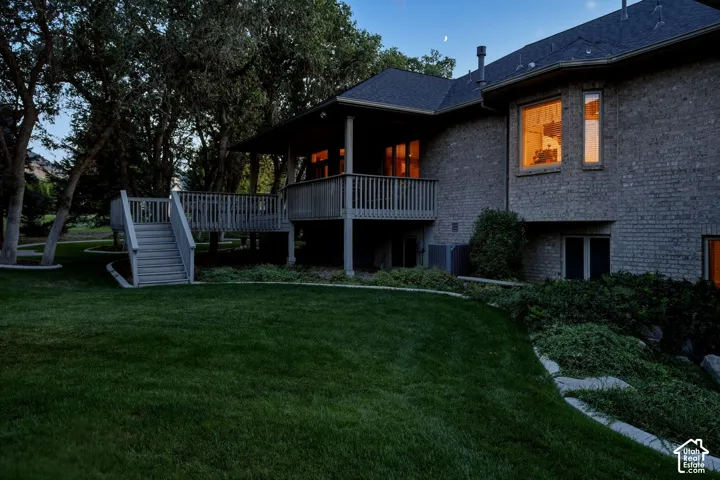 Brick exterior featuring multiple window styles, a raised wood deck with staircase, and sloped, manicured landscaping