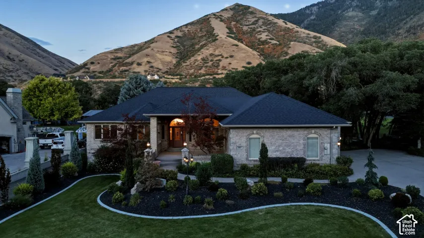 Stone exterior with a dark shingle roof, arched entry, formal landscaping, and a manicured lawn