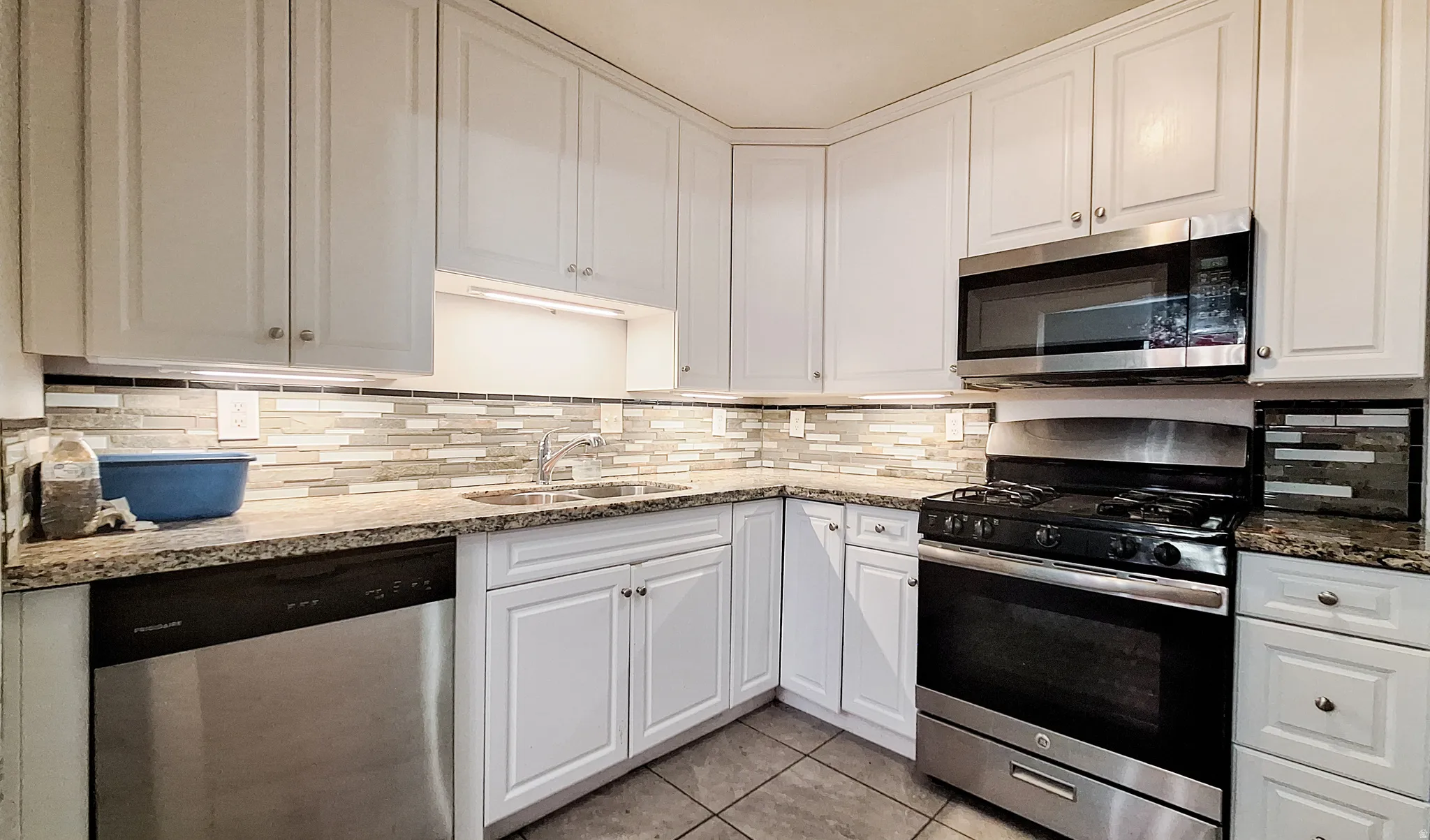 Modern kitchen featuring white cabinetry with brushed nickel hardware, granite countertops, and a linear tile backsplash