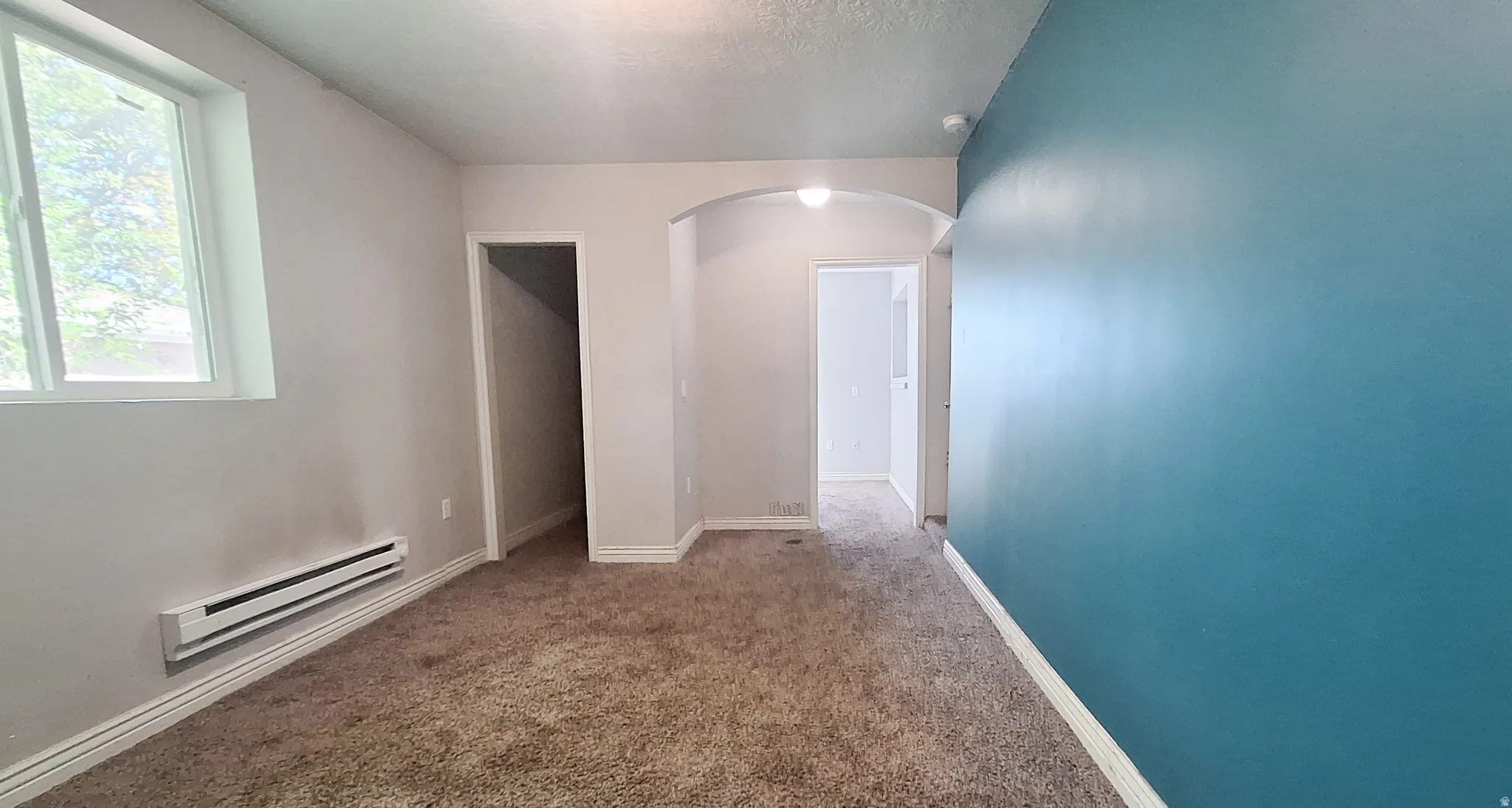 Spacious interior featuring neutral carpeting, curved architectural archway, large window with natural light, accent wall in rich teal, and multiple room openings for flexible layout options
