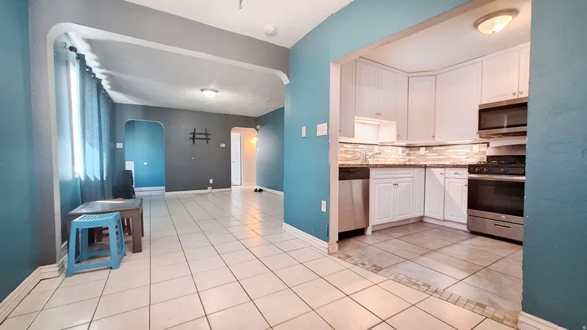 Open-concept kitchen and dining area featuring stainless steel appliances, white cabinetry with ample storage, ceramic tile flooring throughout, recessed lighting, and bright blue accent walls with natural light from multiple windows