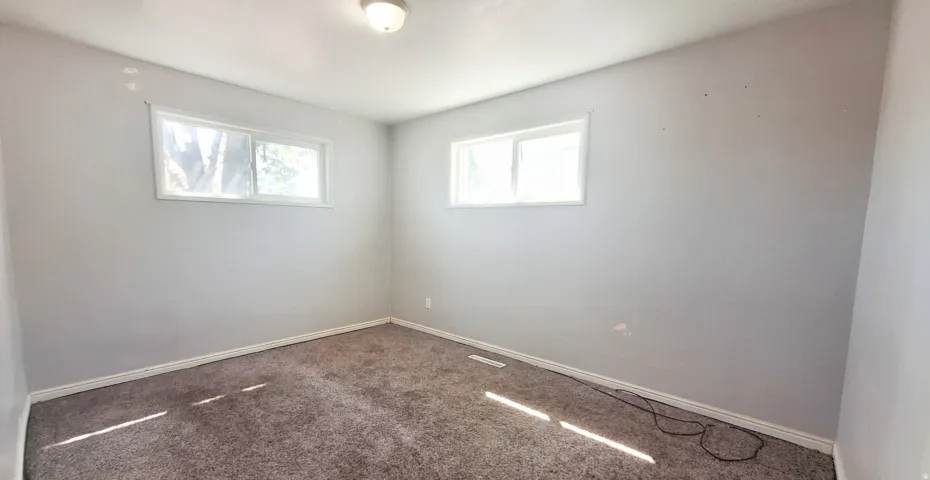 Bright corner bedroom featuring two windows with natural light, neutral wall finishes, and carpet flooring