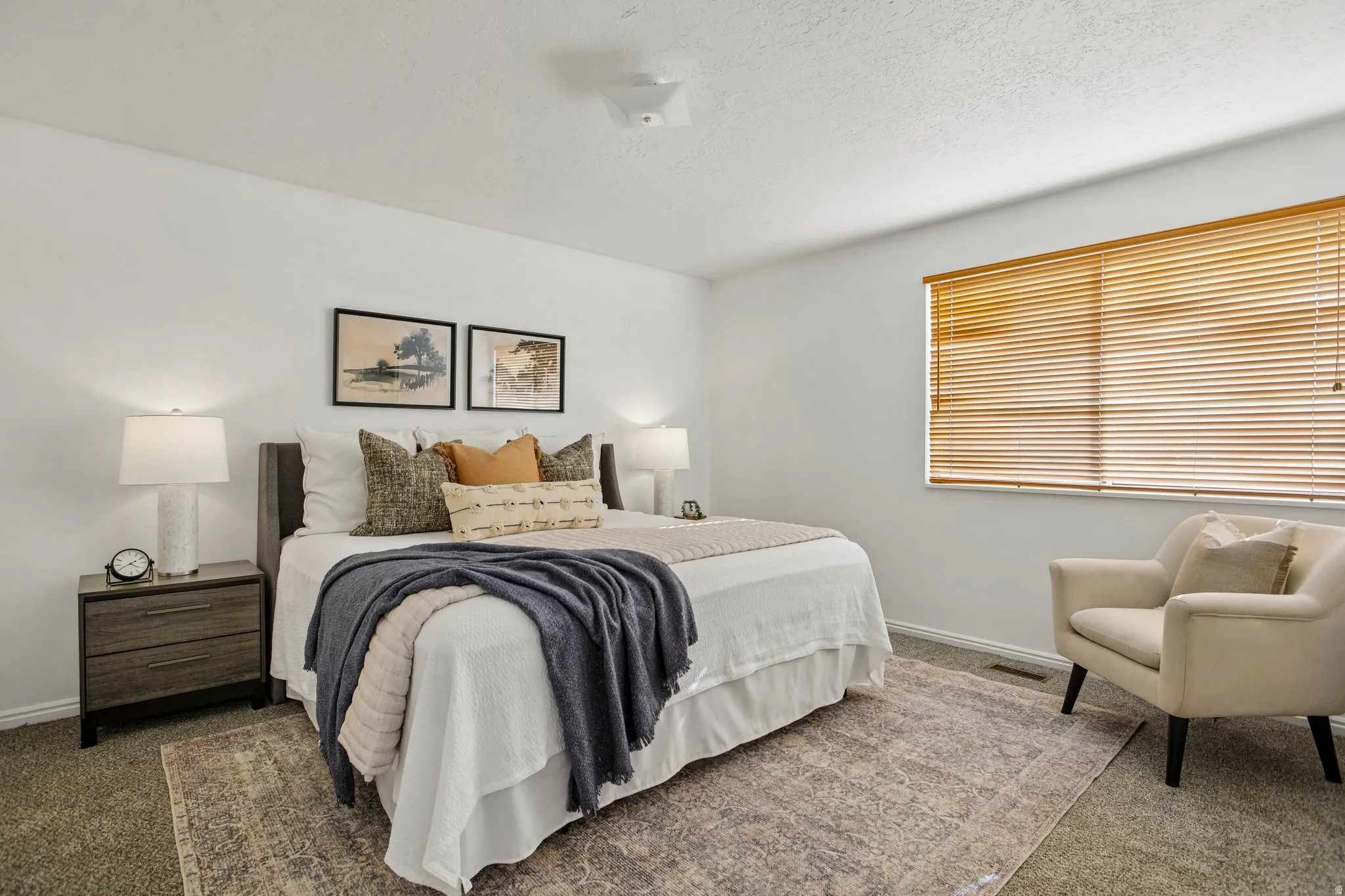 Bedroom with textured carpeting and a large window featuring wood-finish blinds