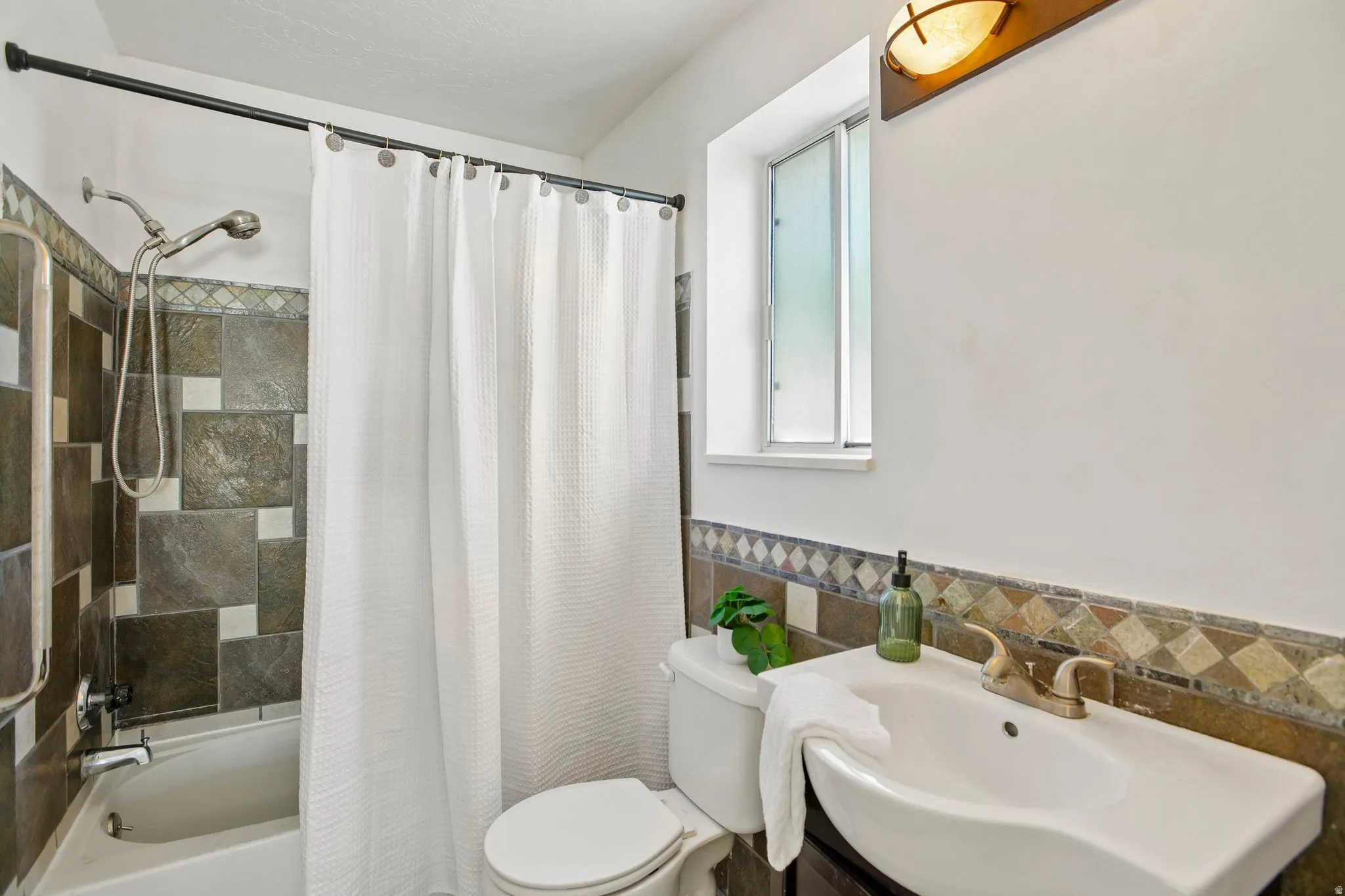 Tiled tub surround with a showerhead, white bathtub, vanity with an integrated sink, and an accent tile backsplash