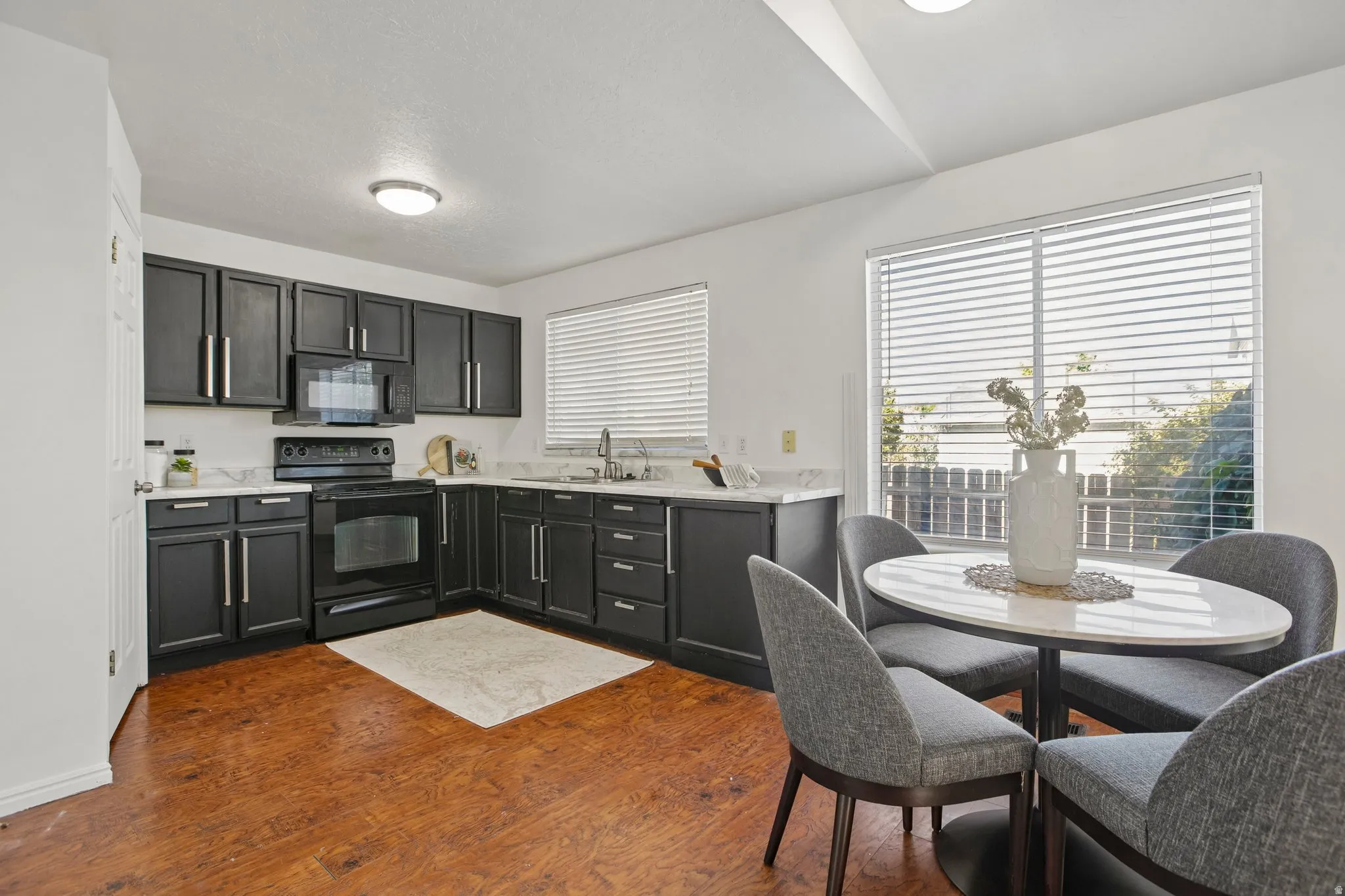 Kitchen featuring dark cabinetry, black appliances, white countertops, wood-finish flooring, and a window with blinds
