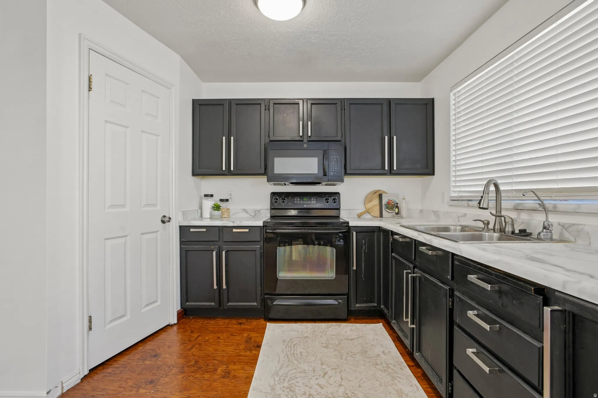 Kitchen featuring dark cabinetry, stainless steel hardware, a stainless steel sink with a gooseneck faucet, light-toned countertops, and wood-finish flooring