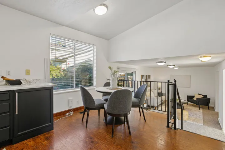 Wood-finish flooring, white walls, black cabinetry with light-toned countertops, large window with blinds, and a black metal railing