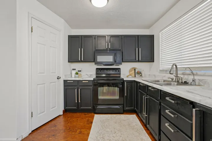 Kitchen featuring dark cabinetry, stainless steel hardware, a stainless steel sink with a gooseneck faucet, light-toned countertops, and wood-finish flooring