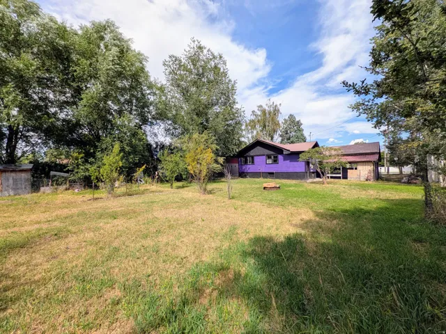 Spacious rural property featuring a vibrant purple residence with attached outbuildings, set on expansive grounds surrounded by mature trees and established landscaping