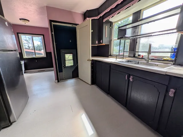 Kitchen with black cabinetry, a stainless steel sink, and white countertops