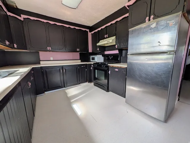 Kitchen featuring black cabinetry, light-colored countertops, a stainless steel refrigerator, a black range, and white flooring