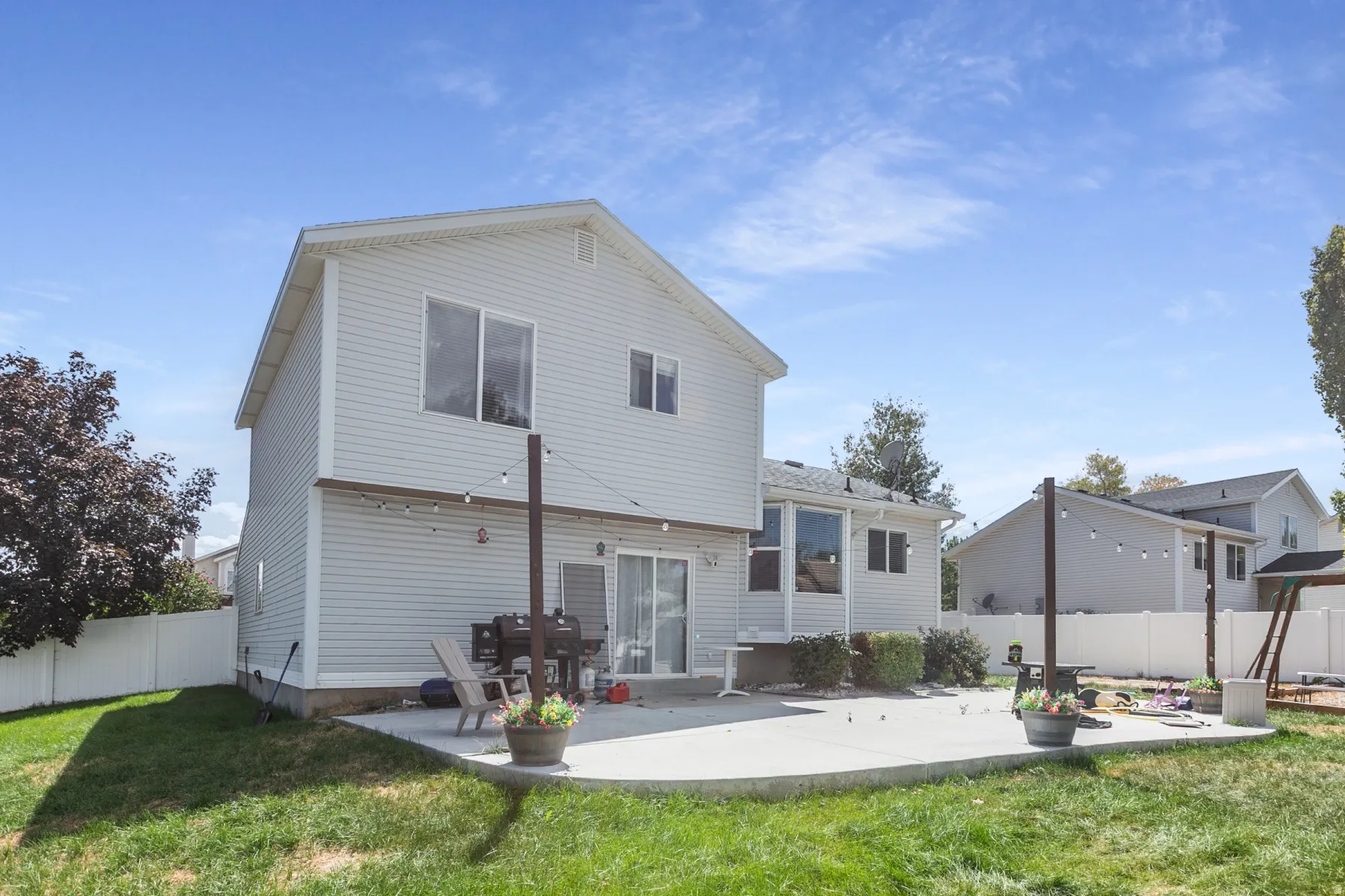 Spacious backyard featuring a concrete patio, white privacy fencing, and mature landscaping