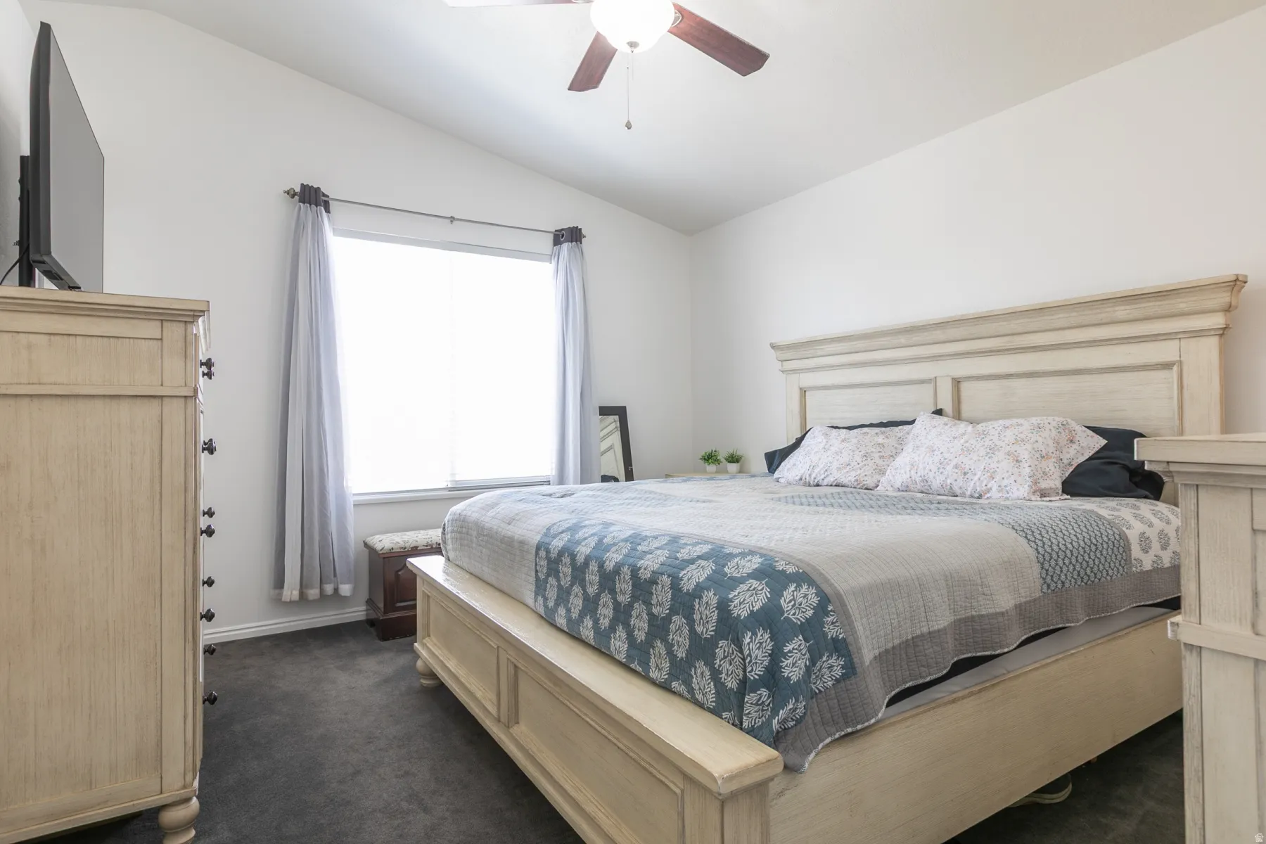 Vaulted ceiling with an attached ceiling fan, large window with blinds, and dark gray carpet flooring