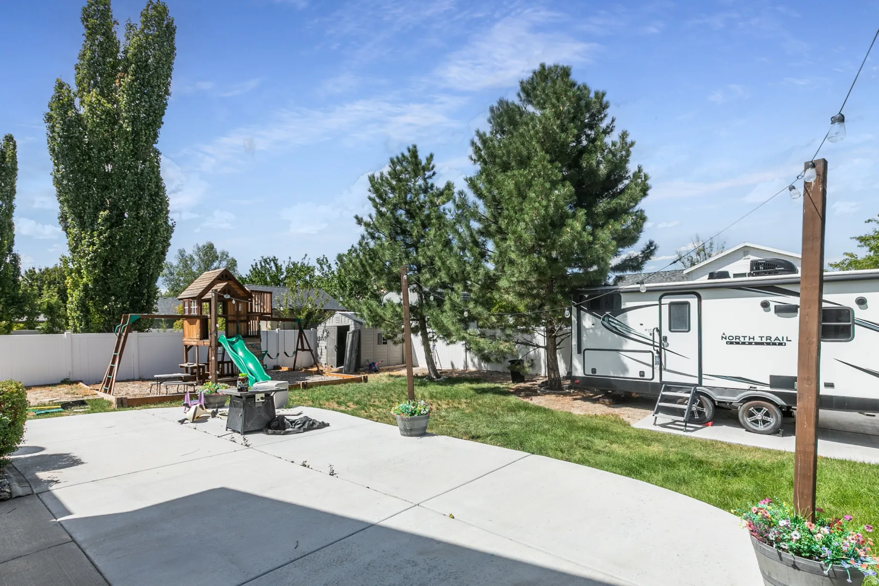 Expansive backyard featuring a concrete patio, green lawn, privacy fencing, and mature trees