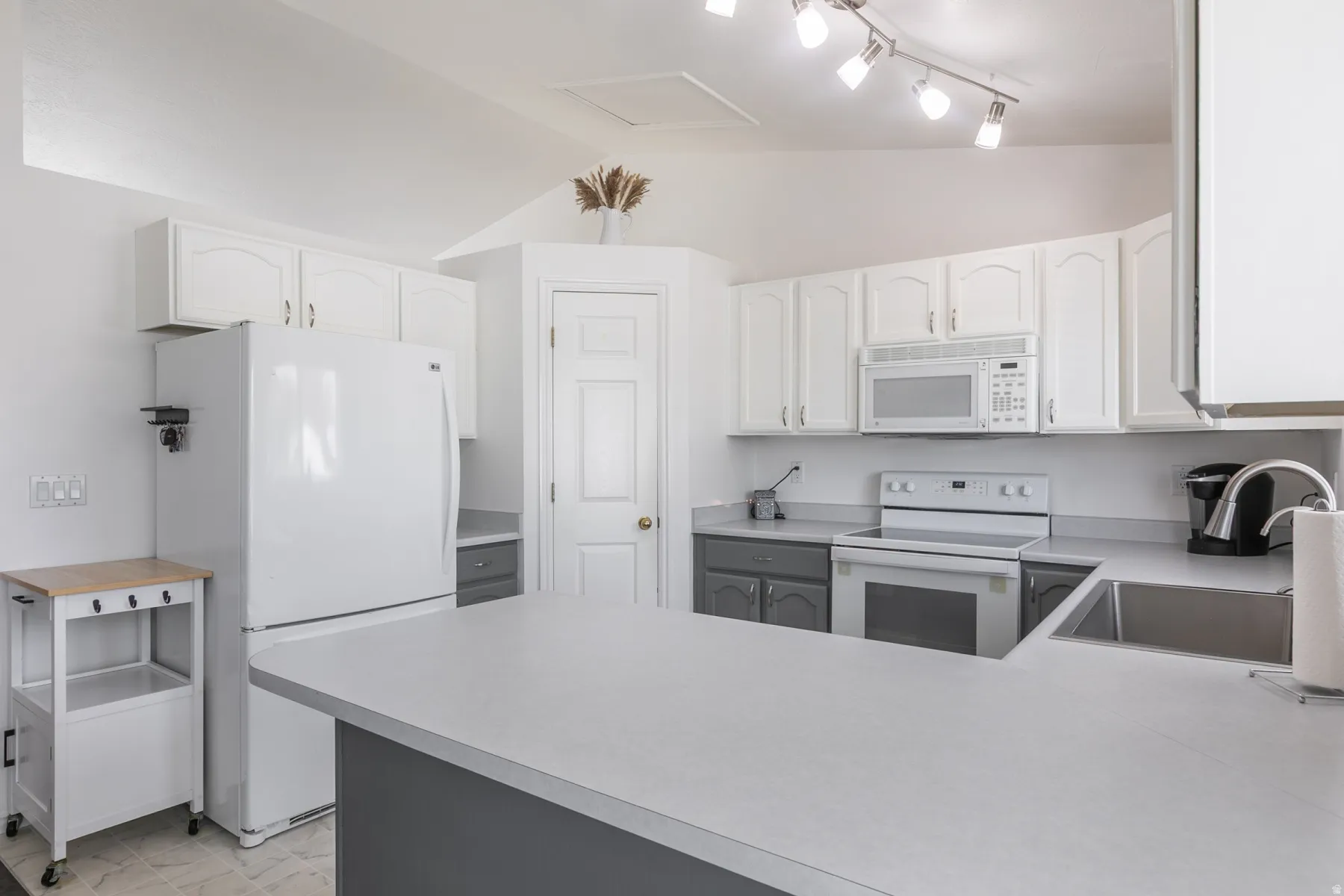 Kitchen featuring a U-shaped island, white cabinetry, integrated stainless-steel sink, and track lighting