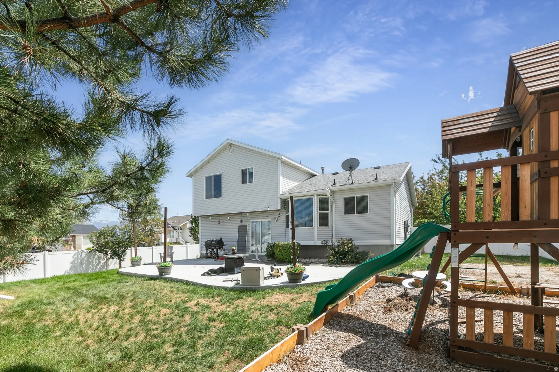Expansive backyard featuring a multi-level concrete patio, mature trees, and white privacy fencing