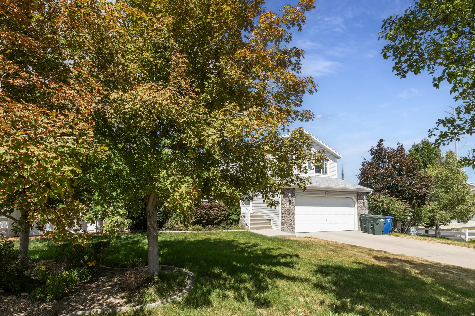 Two-story residence featuring light gray siding with stone-clad accents and a two-car garage