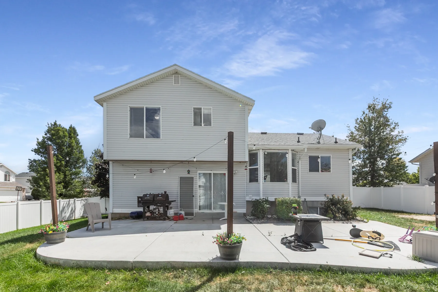 Expansive concrete patio with a sliding glass door, white vinyl siding, and a white privacy fence