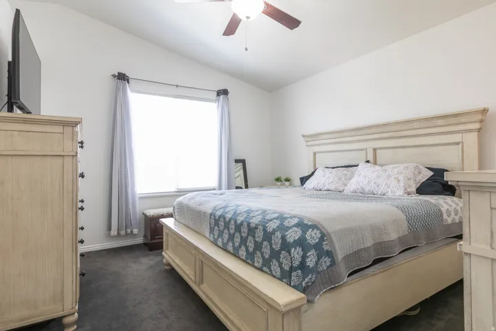 Vaulted ceiling with an attached ceiling fan, large window with blinds, and dark gray carpet flooring