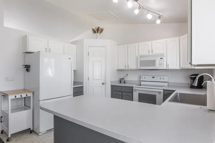 Kitchen featuring a U-shaped island, white cabinetry, integrated stainless-steel sink, and track lighting