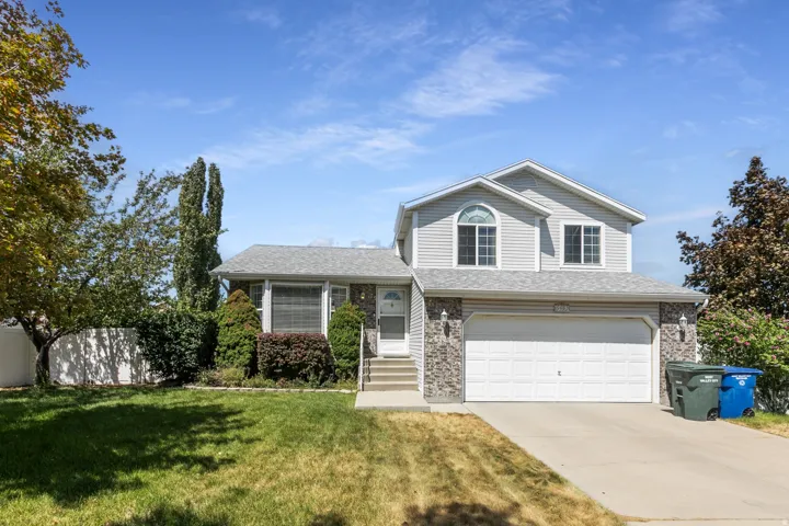 Two-story residence featuring light gray siding, a stone veneer facade, a two-car garage, and a concrete driveway