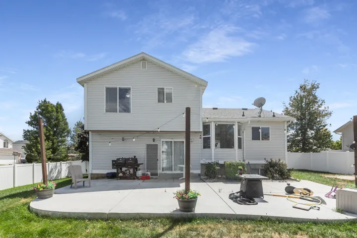 Expansive concrete patio with a sliding glass door, white vinyl siding, and a white privacy fence
