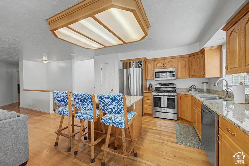 Kitchen featuring wood cabinetry, stainless steel appliances, granite countertops, a center island with seating, and wood flooring