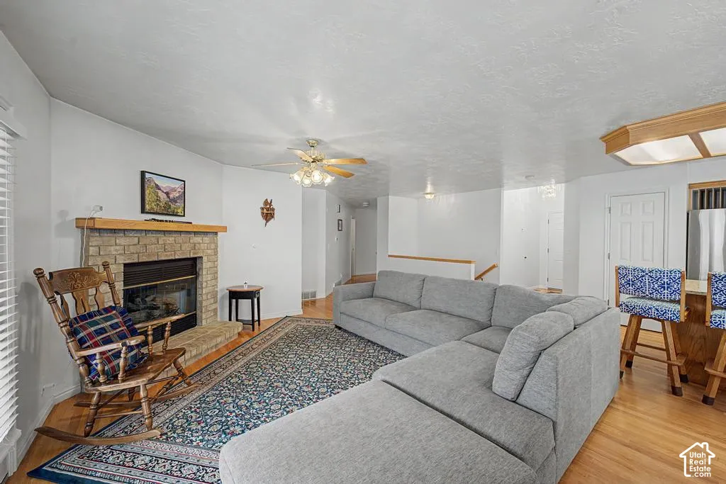 Brick-surround fireplace with a wood mantle, hardwood flooring, and a ceiling fan with integrated lighting