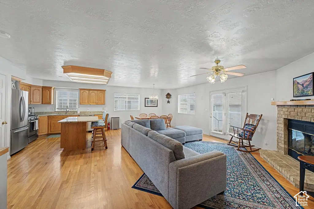 Open-concept living space featuring hardwood floors, a kitchen island with seating, a fireplace with a stone surround, and French doors